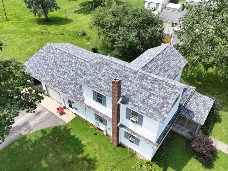 A finished light gray architectural shingle roof on a two-story home, from the drone