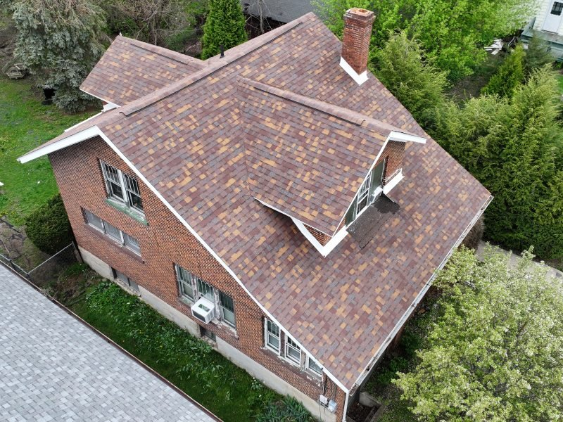 A brick two-story home with a new blended brown shingle roof, from the drone