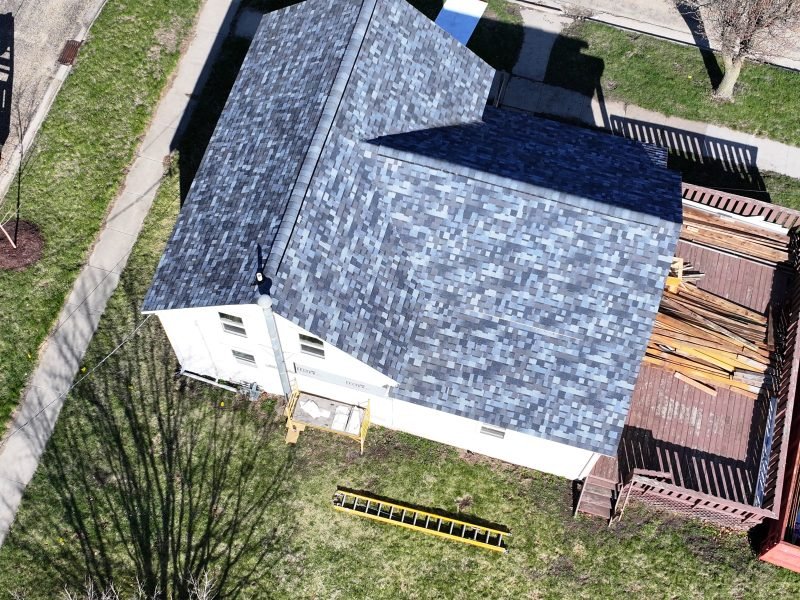 A roof mid-replacement: blue synthetic underlayment laid, new gray shingles going on