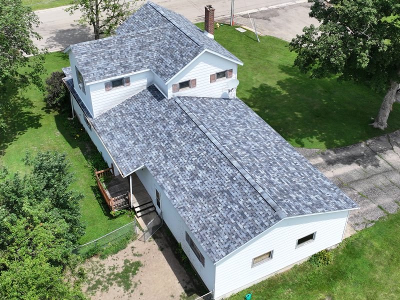 The finished light gray roof and white house seen from the street side by the drone