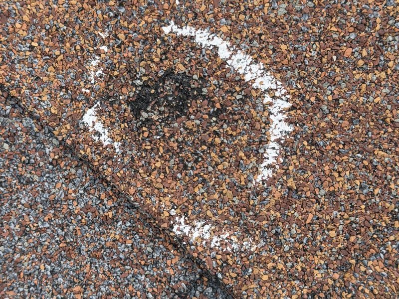 A hail hit on an asphalt shingle, circled in chalk during one of our inspections